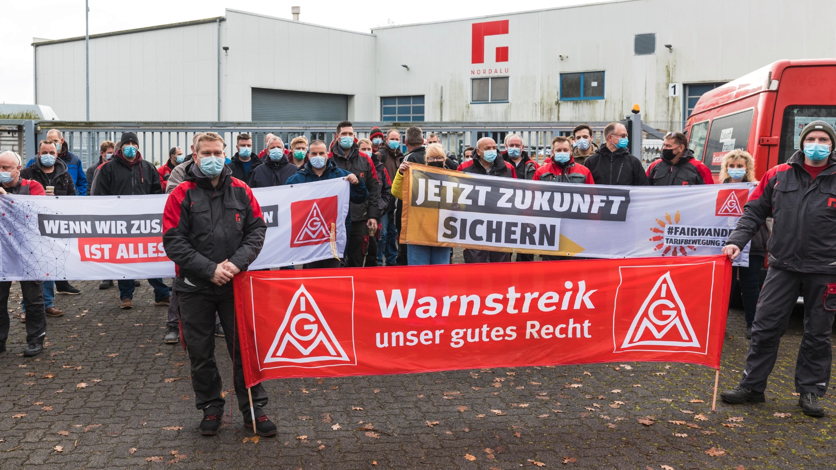 Streikende Metaller:innen mit Transparenten vor dem Tor der Firma Nordalu